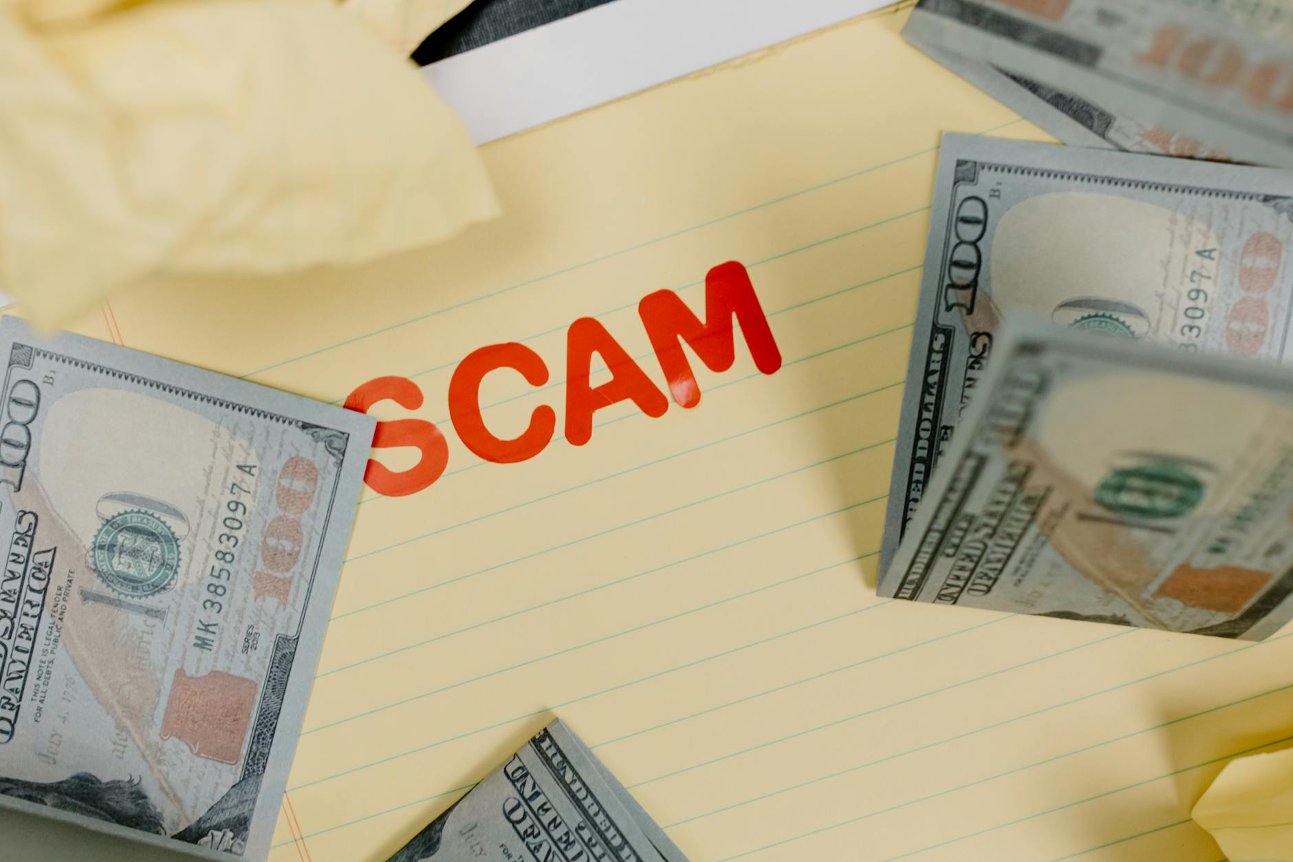 Banknoty dolarowe na żółtym tle z napisem scam jako symbol oszustwa