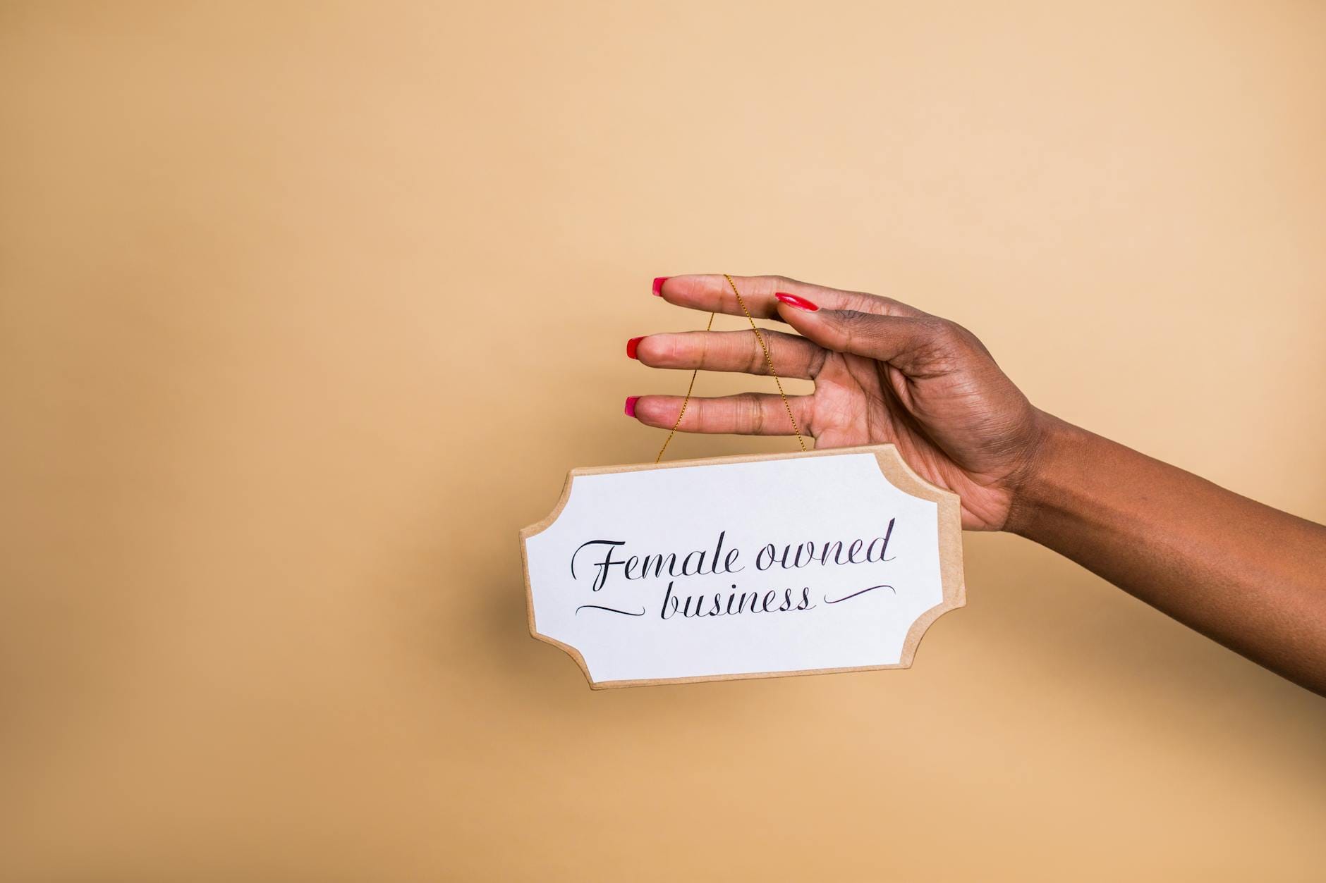 Dłoń kobiety trzymająca tabliczkę Female Owned Business na beżowym tle