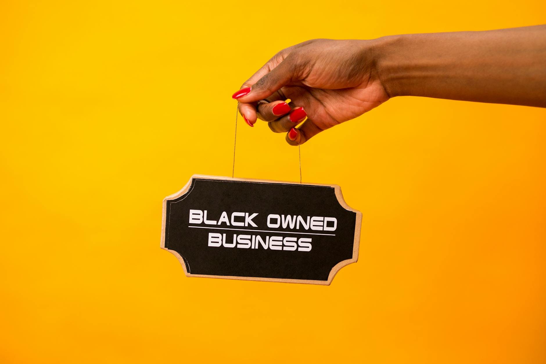 Dłoń trzyma szyld Black owned business na żółtym tle