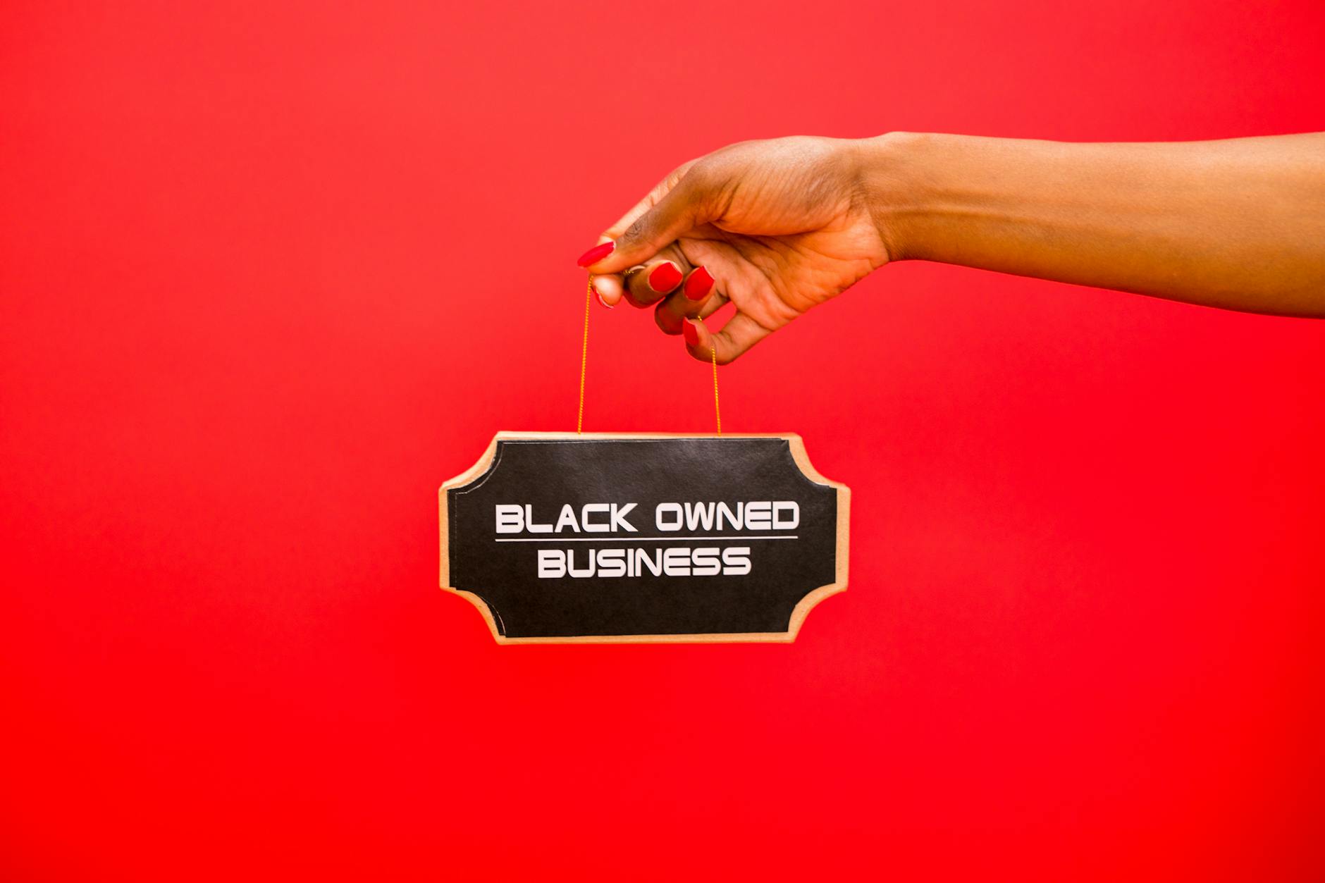 Dłoń trzymająca tabliczkę z napisem Black Owned Business na czerwonym tle