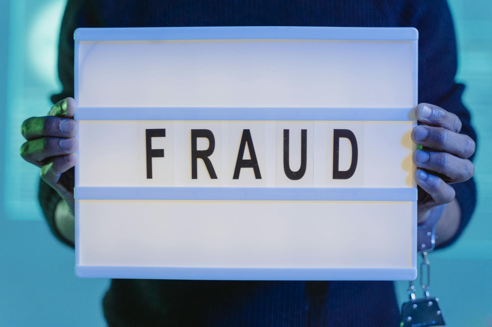Dłonie trzymające podświetloną na niebiesko tabliczkę z napisem fraud