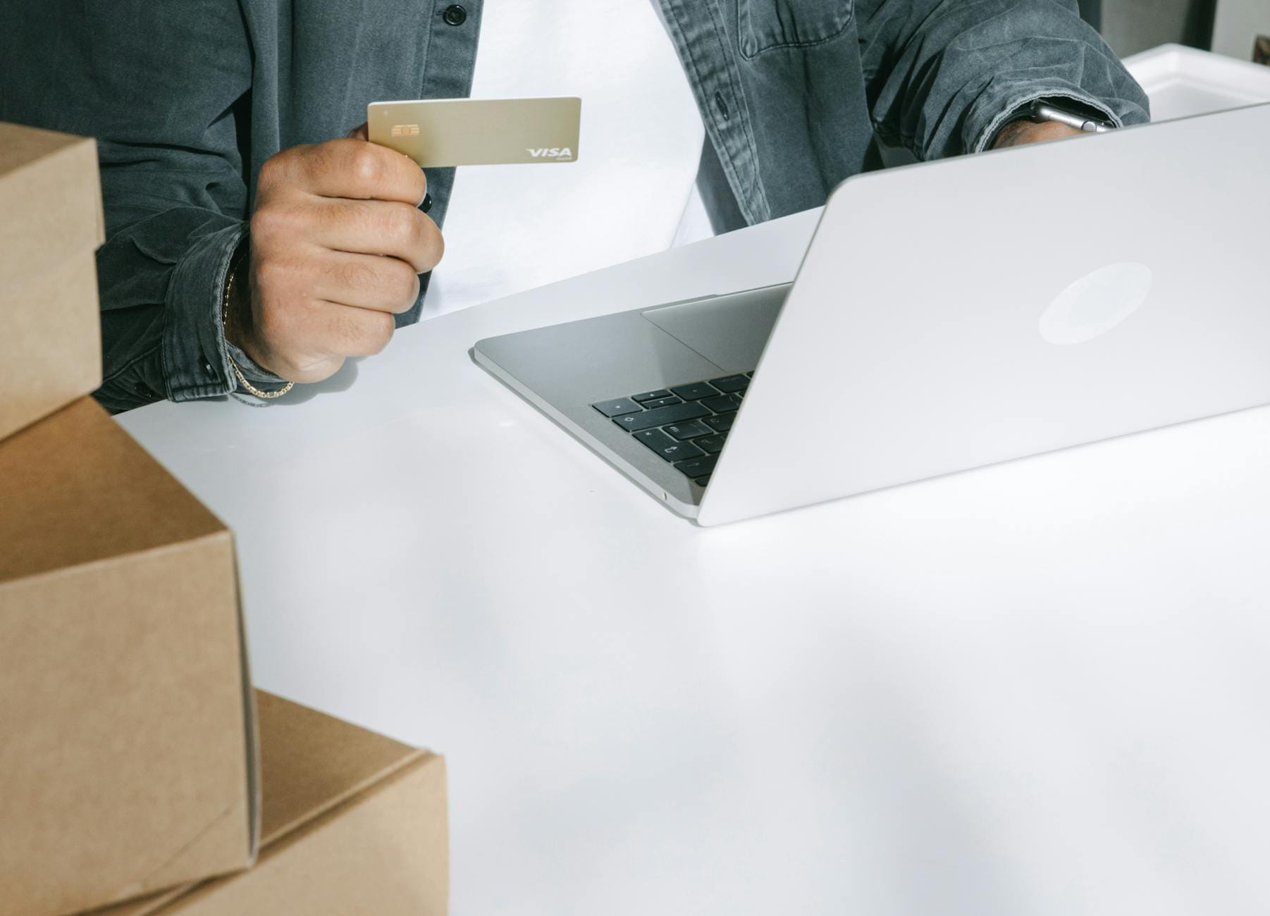 Osoba płaci kartą za zakupy online na laptopie wśród pudełek wysyłkowych