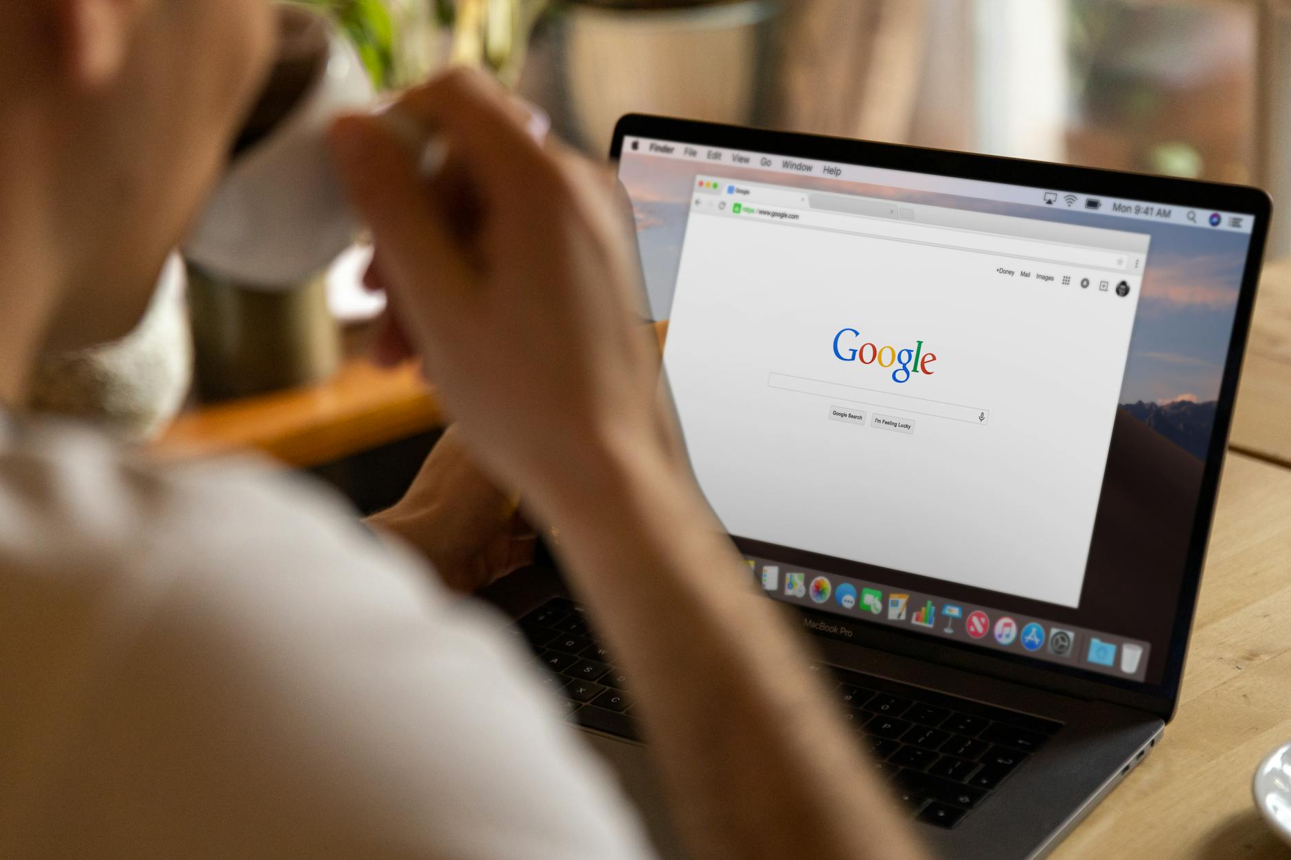 Osoba przy laptopie szukająca informacji w Google przy kawie