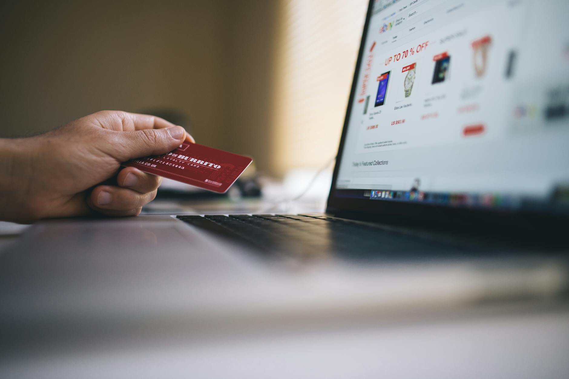 Osoba trzymająca kartę płatniczą przed laptopem podczas zakupów online