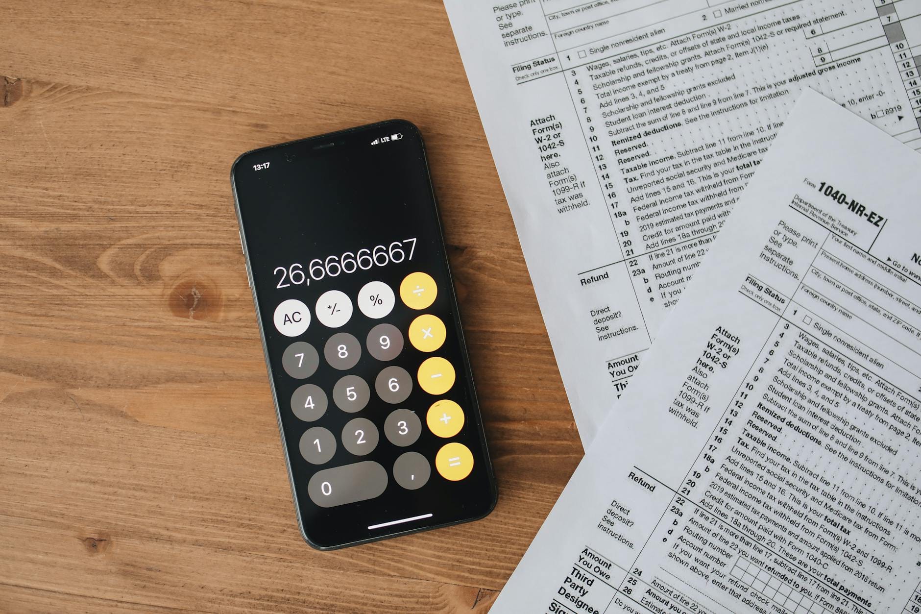 Smartfon z kalkulatorem obok formularzy podatkowych na drewnianym stole