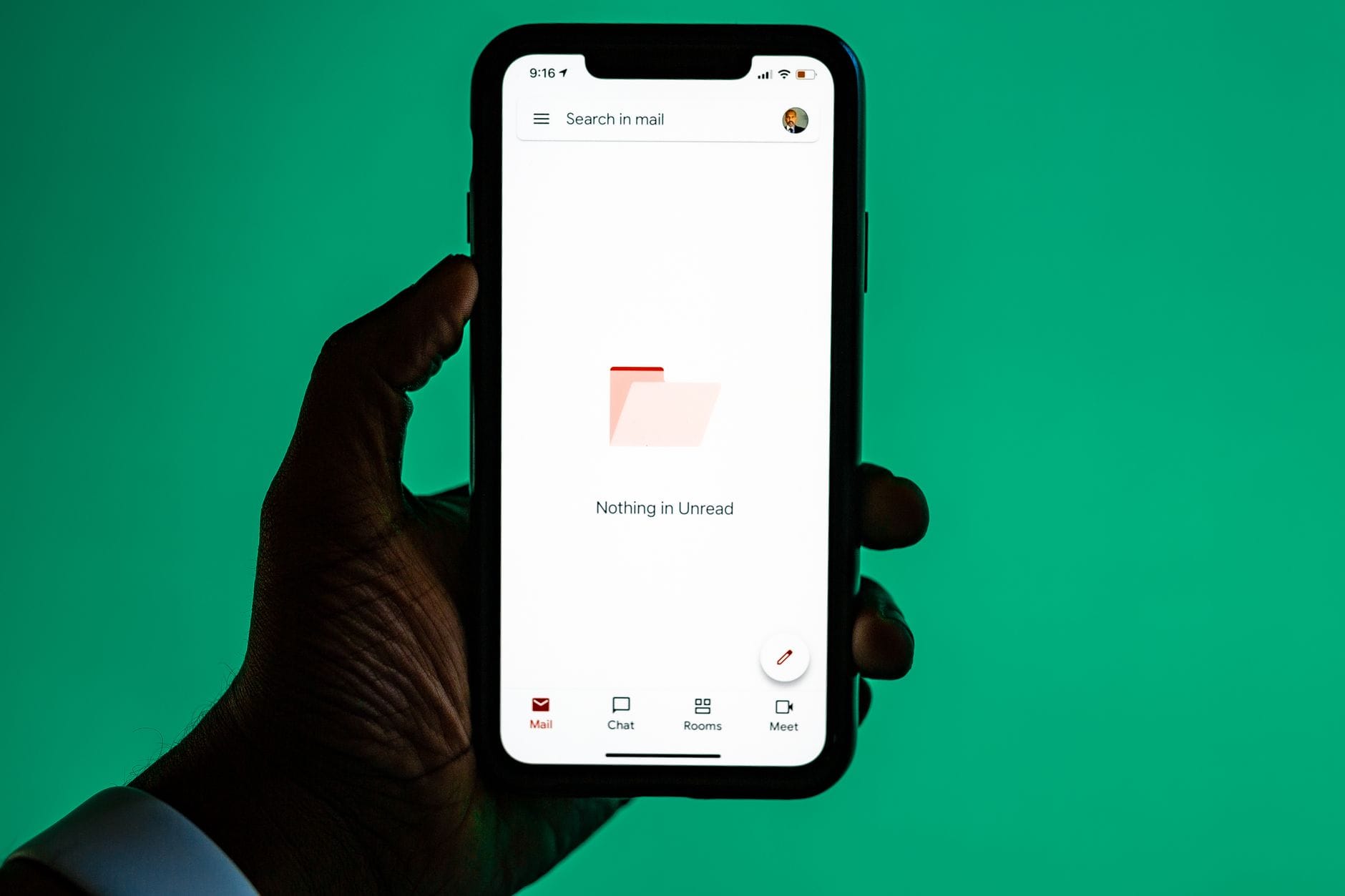 Dłoń trzymająca smartfon z otwartą aplikacją e-mail na zielonym tle