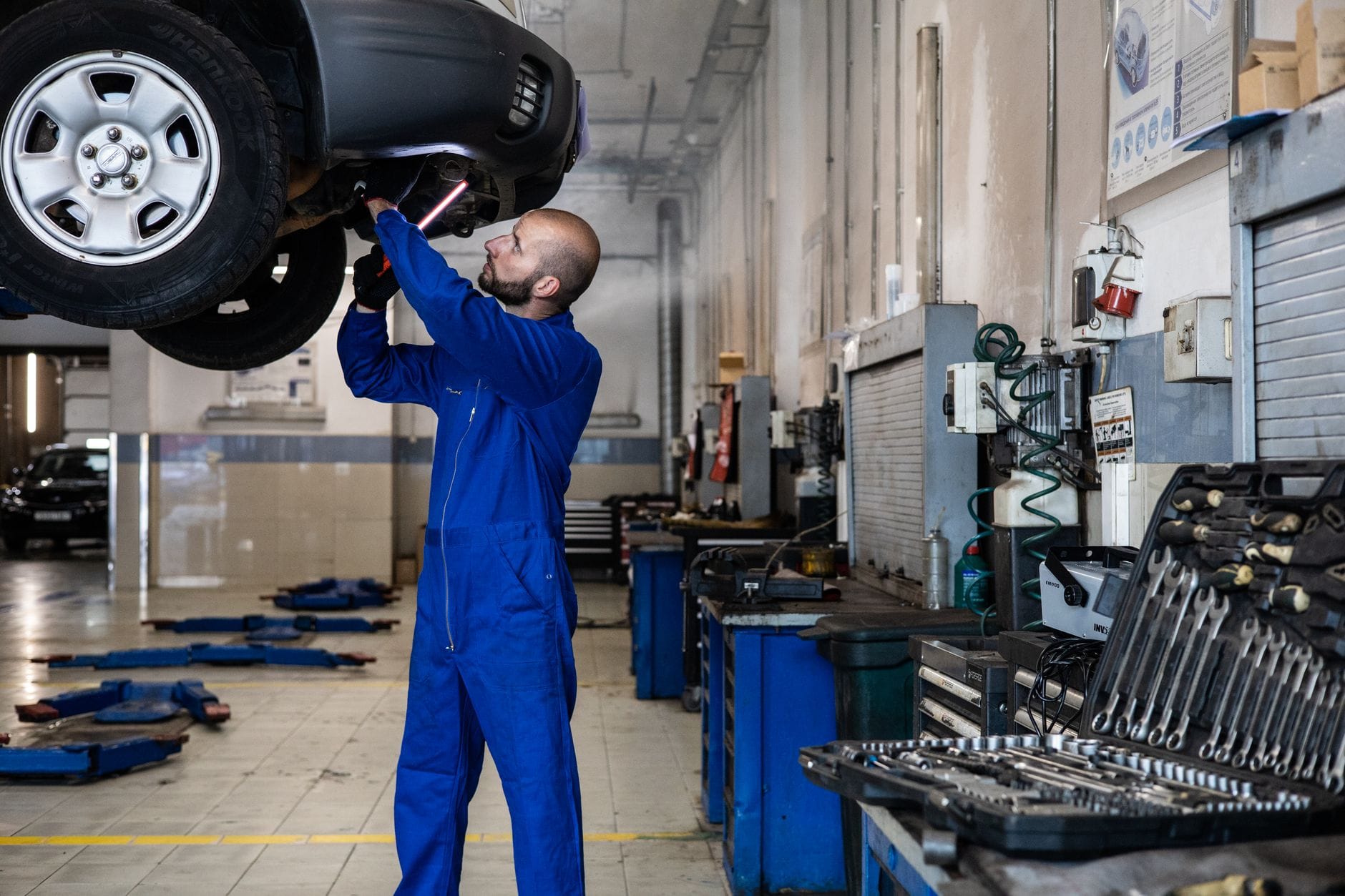 Mechanik sprawdza podniesiony samochód na podnośniku w warsztacie