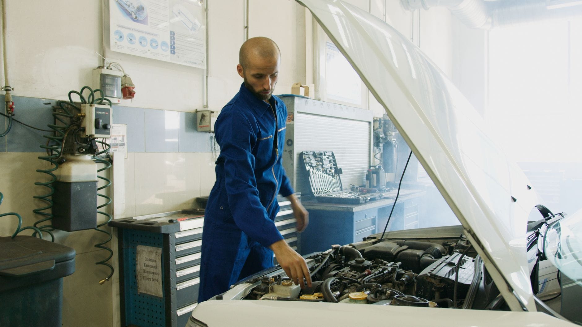 Mechanik w niebieskim kombinezonie sprawdza silnik Mazdy w warsztacie