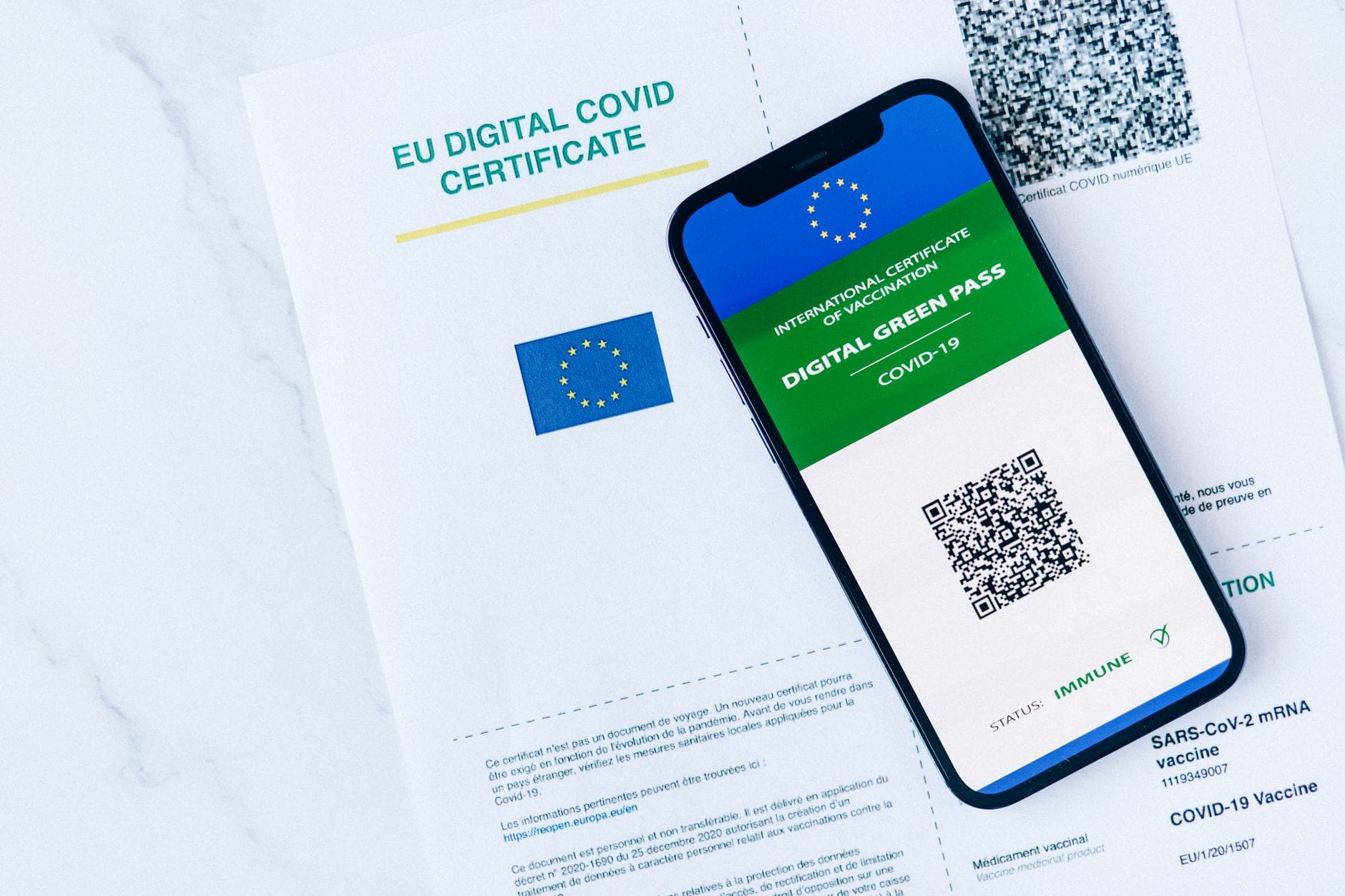 Certyfikat covidowy UE na smartfonie obok papierowego zaświadczenia