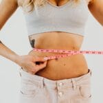 Kobieta w sportowym staniku mierzy talię różową miarką centymetrową