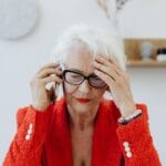 Starsza kobieta w czerwonej marynarce zestresowana rozmową telefoniczną